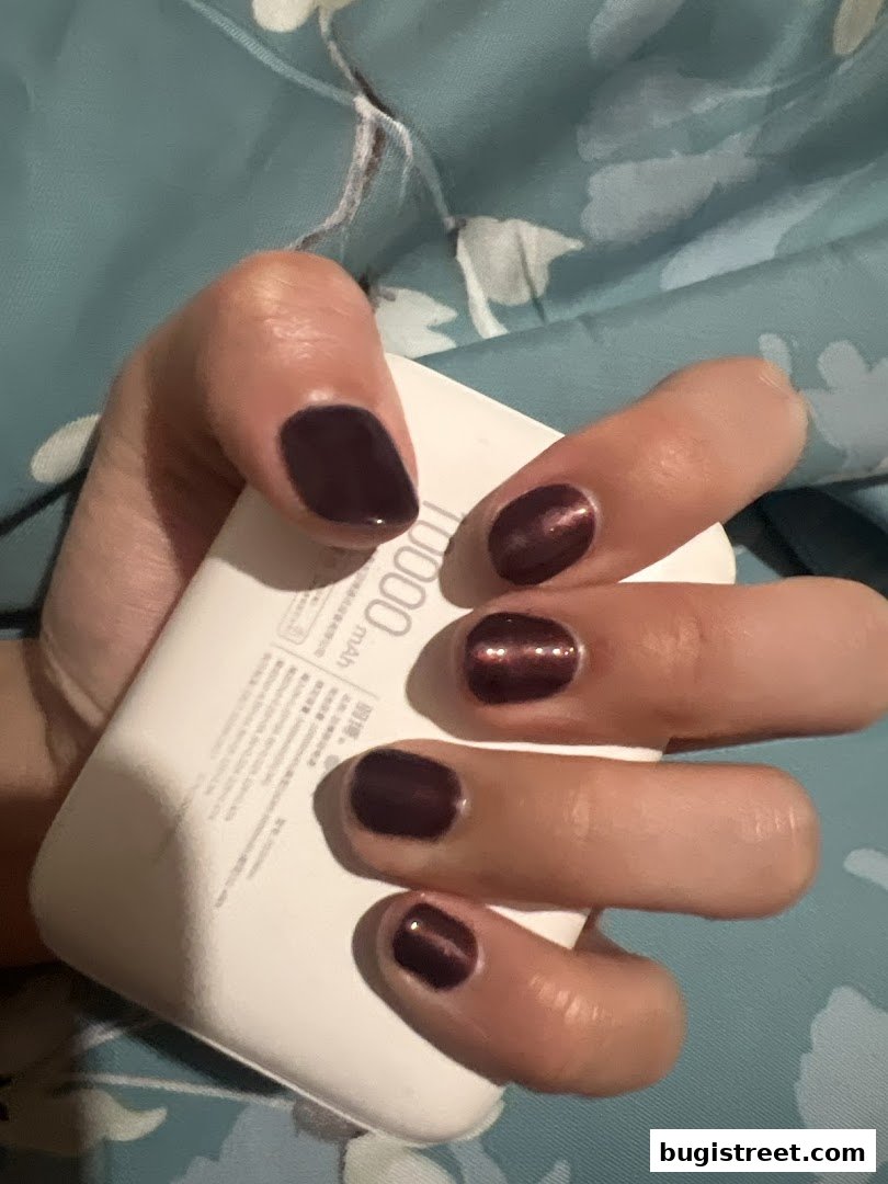 A hand with dark, glossy nail polish holds a white portable charger.