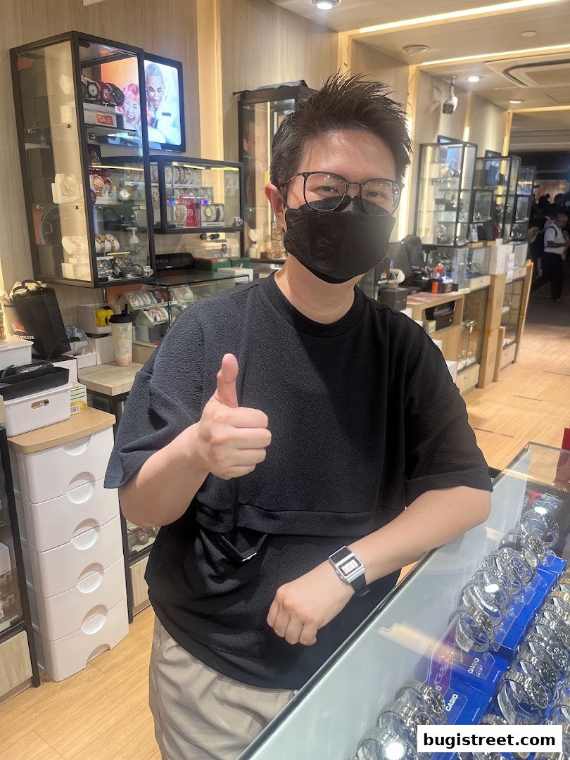 A person wearing a mask and giving a thumbs up in a watch shop.