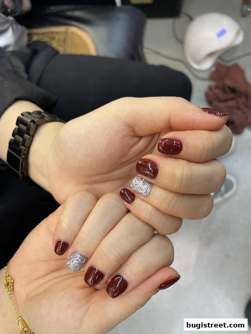 Close-up of hands with a fresh manicure featuring dark red polish and glitter accents.