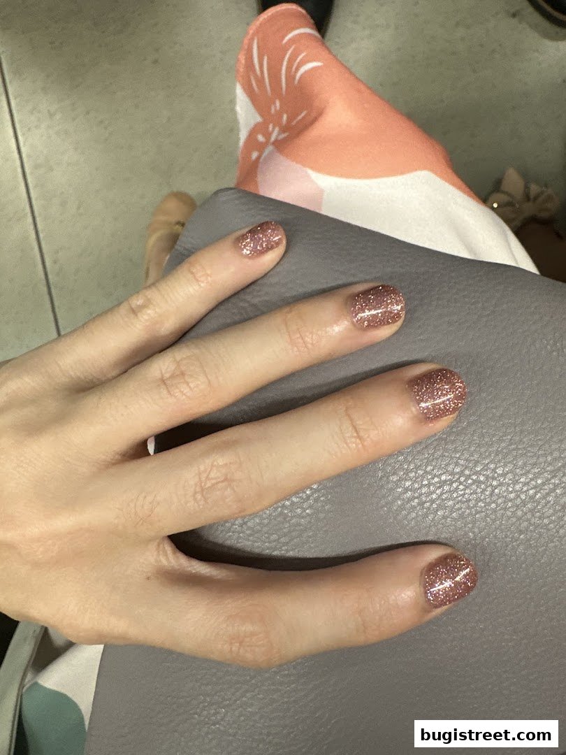 A close-up of a hand with glittery rose gold nails resting on a grey surface.
