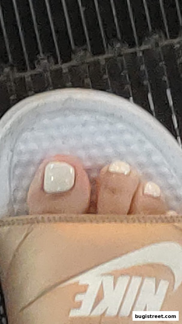 A close-up of a person's toes with white nail polish, wearing a sandal.