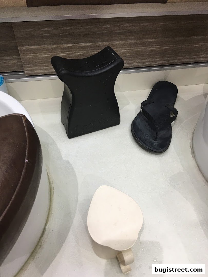 Nail spa equipment including a black footrest, a black flip-flop, and a white cup.