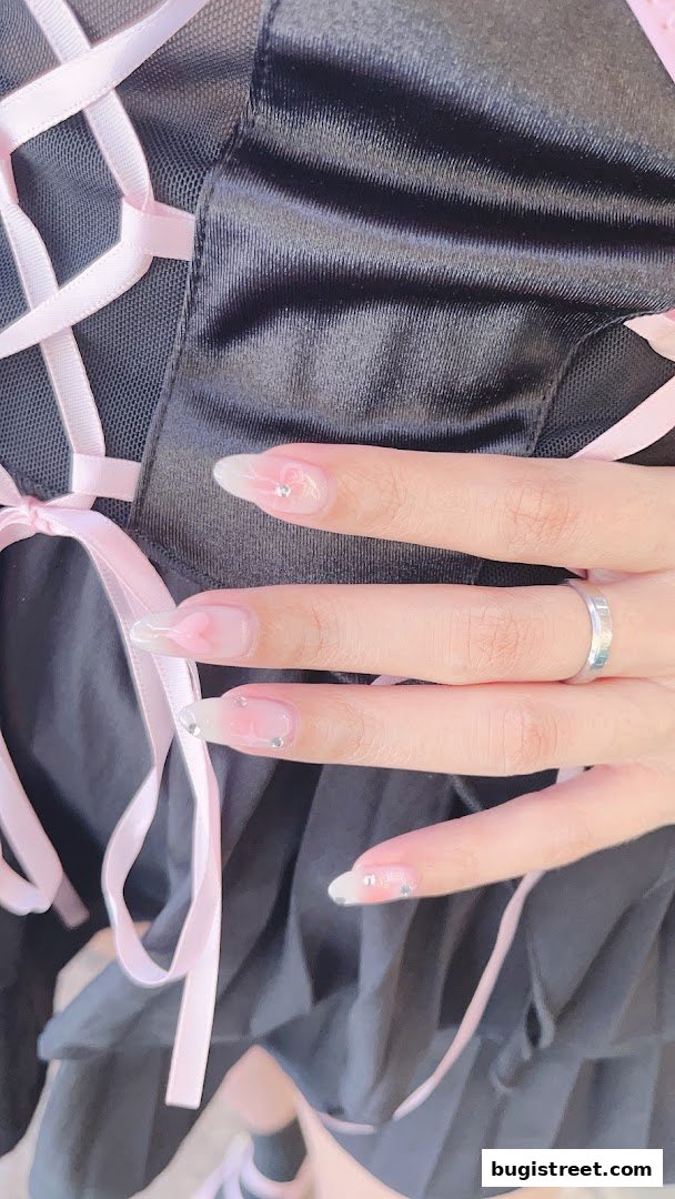 Close-up of a hand with delicate, light pink and clear gel nails adorned with small rhinestones.