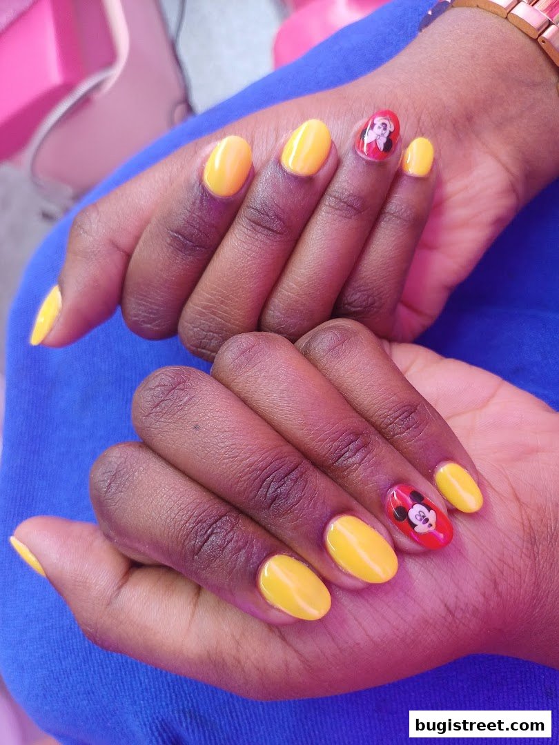 Close-up of hands with bright yellow oval nails, some featuring Mickey Mouse designs.