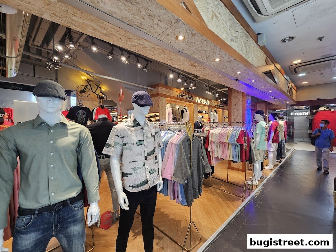 Mannequins display casual wear inside a clothing store with racks of t-shirts.