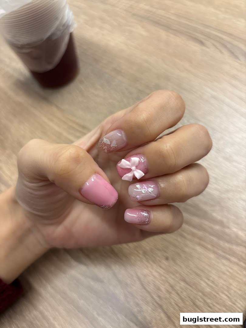 A close-up of a hand with beautifully decorated pink nails featuring glitter and a small bow.