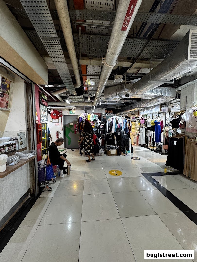 A shopping aisle with various clothing stores and a person sitting on a cart.