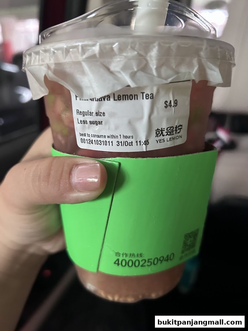 A hand holds a cup of Guava Lemon Tea with a green sleeve from YES LEMON.