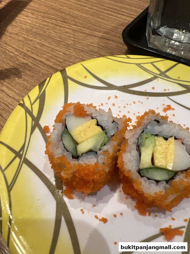 Close-up of two California rolls on a decorative plate with a glass of water in the background.