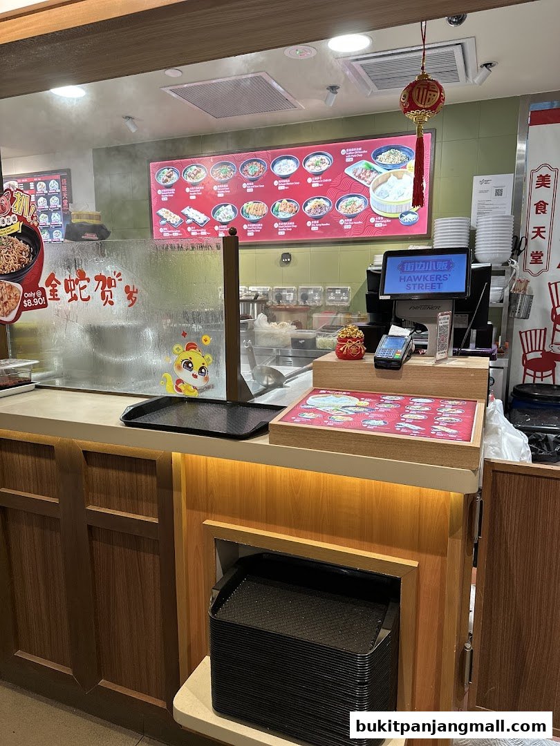 A food stall counter with a digital menu board displaying various dishes and a payment terminal.