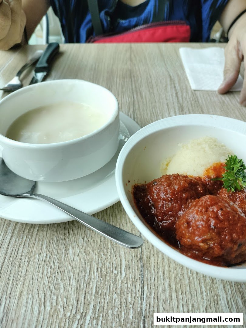 A close-up of a meal with meatballs in sauce and a bowl of soup on a wooden table.