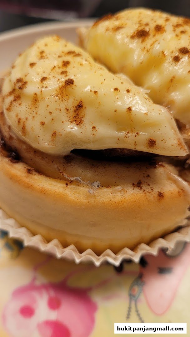 A close-up of a cinnamon roll topped with creamy frosting and a sprinkle of cinnamon.