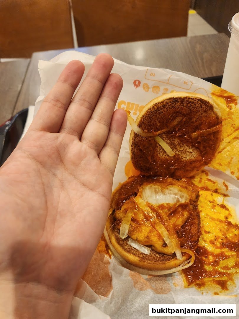A hand is shown next to a partially eaten burger with onions and sauce.