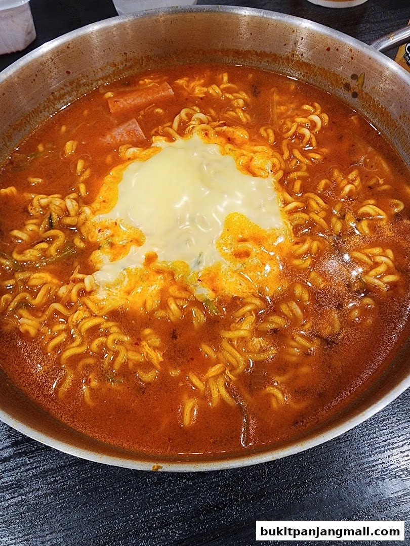 A close-up shot of a steaming bowl of Korean ramen with melted cheese and sausage.