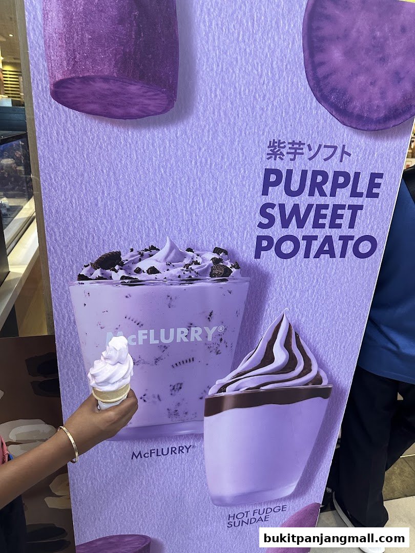 A person holds a purple sweet potato ice cream cone in front of a promotional poster.
