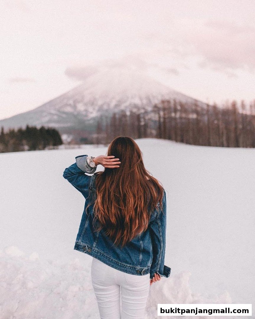 A woman with long brown hair in a denim jacket stands in a snowy landscape.