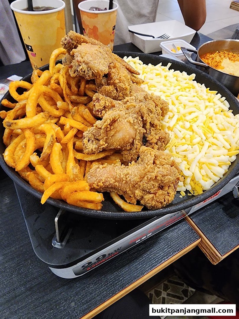 A platter of fried chicken, curly fries, and shredded cheese, with drinks in the background.