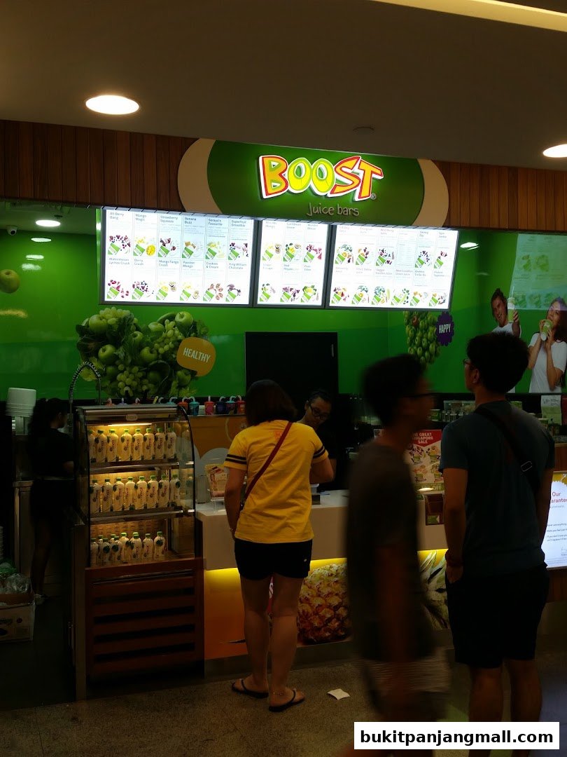 Customers ordering at a Boost Juice bar with a menu board and chilled drinks display.