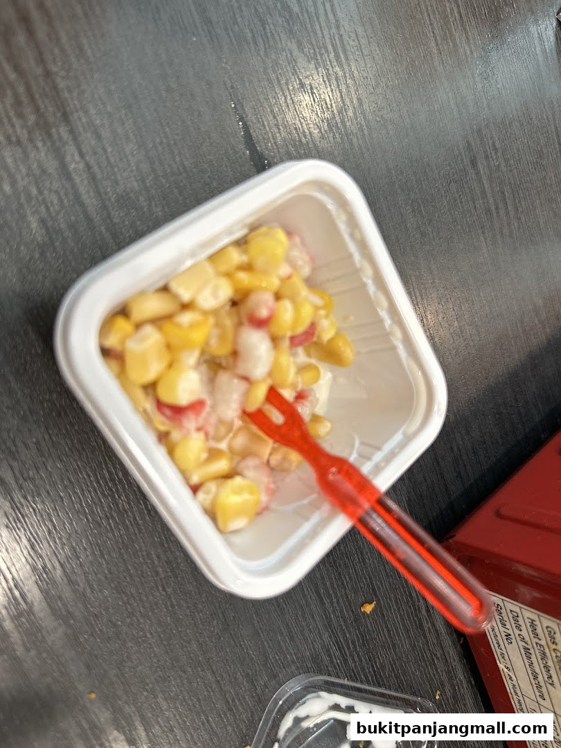 A white container filled with corn and other ingredients, with a red fork inside.