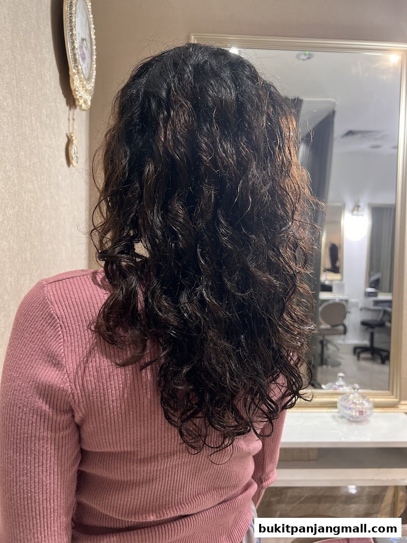 A person with long, curly, dark hair seen from behind in a salon.