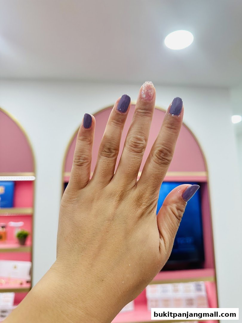 A hand with purple nail polish, showing one nail with glittery polish.