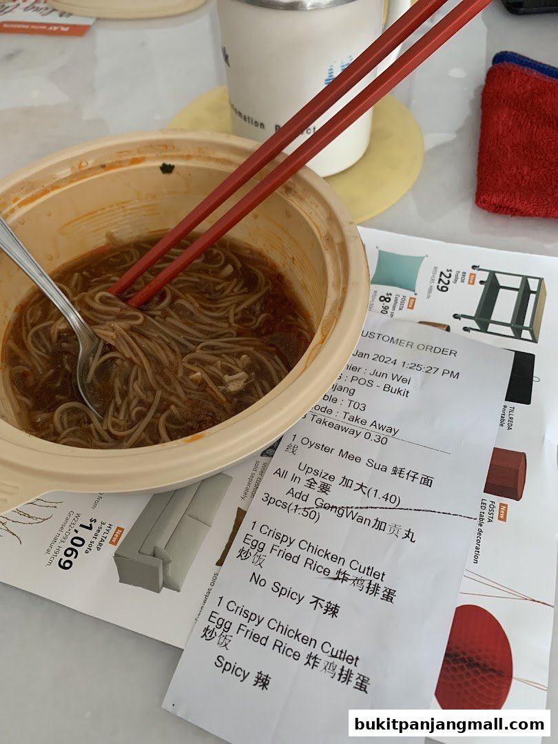 A bowl of noodles with chopsticks and a customer order receipt.