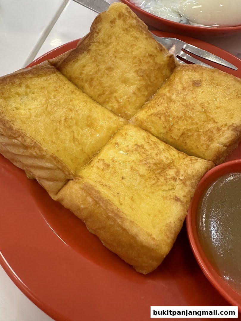 A close-up of golden-brown kaya toast served on a red plate with a side of kaya dip.