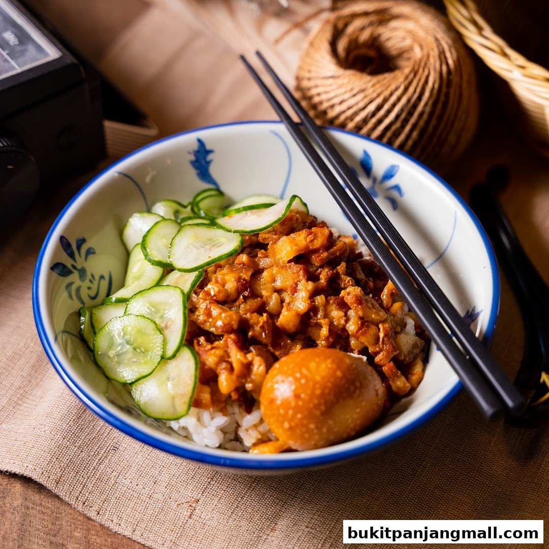 A close-up of a bowl of rice topped with braised pork, sliced cucumbers, and a braised egg.