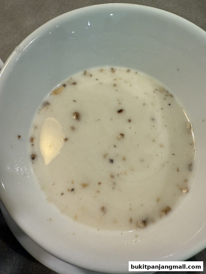 A close-up shot of a white bowl filled with a creamy soup with small pieces of food.