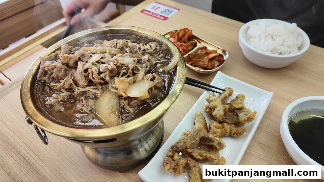 A steaming bowl of beef bibimbap with kimchi, fried meat, rice, and soup.