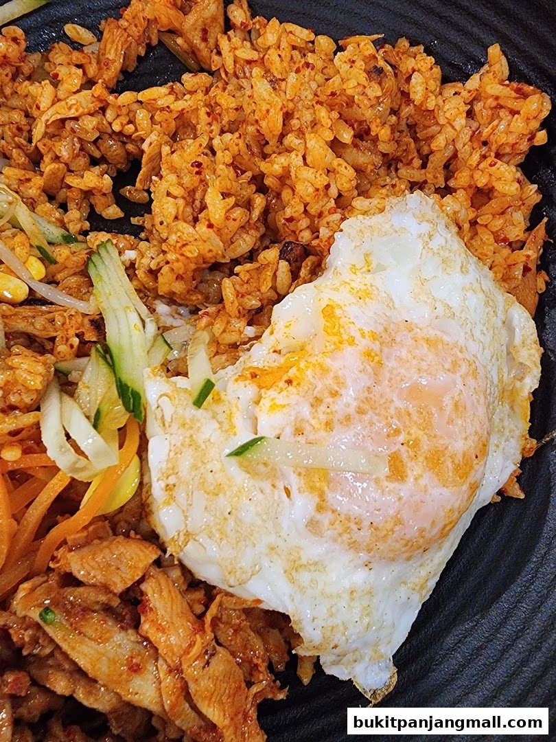 A close-up of a Korean dish with fried rice, meat, vegetables, and a fried egg.