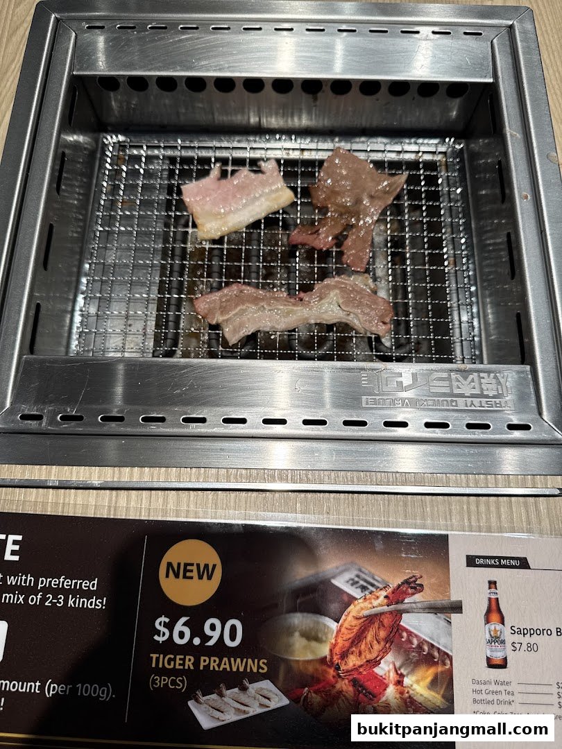 Meat grilling on a Yakiniku grill with a menu featuring tiger prawns and drinks.
