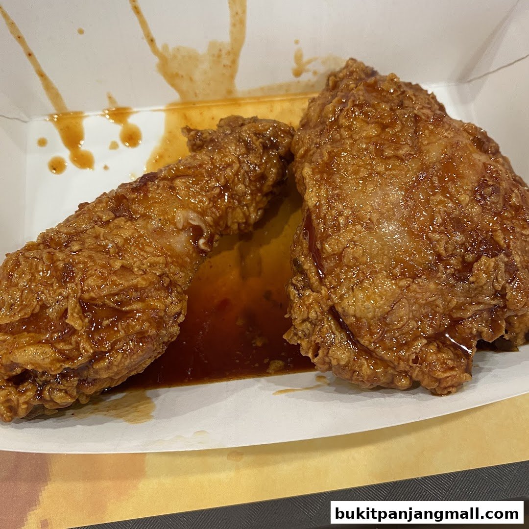 Two pieces of crispy fried chicken coated in a glossy sauce in a takeaway box.