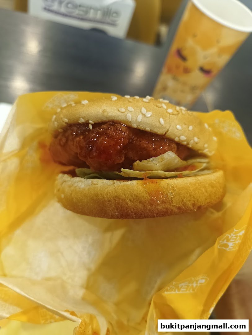 A close-up shot of a delicious NeNe Chicken burger with a drink in the background.