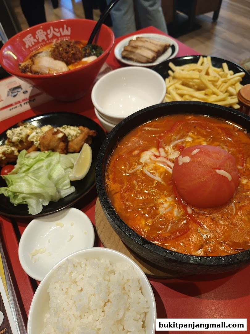 A table filled with various Japanese dishes including ramen, fried chicken, fries, and rice.
