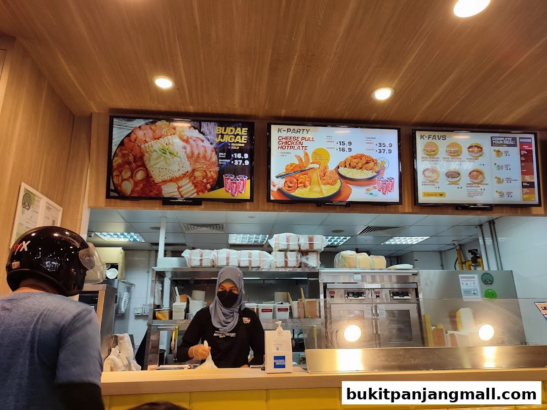 A view of a NeNe Chicken counter with digital menus displaying Korean food items.