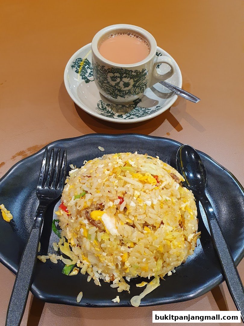 A plate of fried rice with a cup of tea on a saucer, served with cutlery.