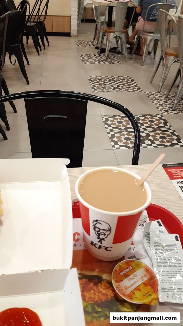 A close-up of a KFC meal with a drink and a small container of maple syrup.