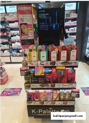 A display stand featuring K-Palette makeup products and other beauty items in a Watsons store.