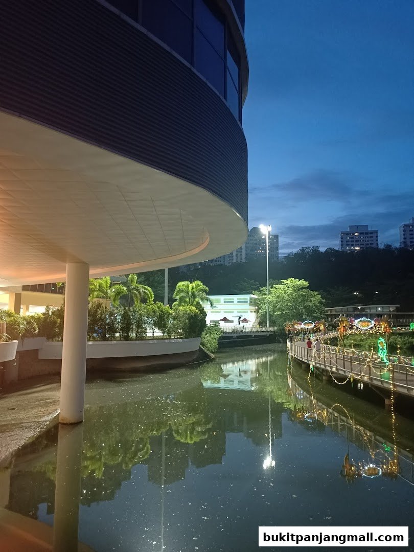 A scenic view of a library's exterior with a water feature and illuminated walkway at dusk.