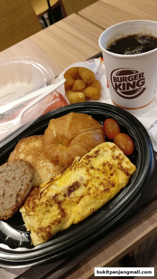 A Burger King breakfast meal with an omelet, croissant, sausage, tater tots, and a drink.