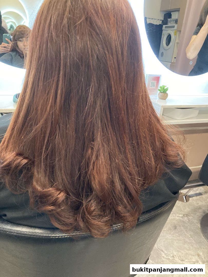 A person's long, reddish-brown hair styled with gentle curls, viewed from behind.