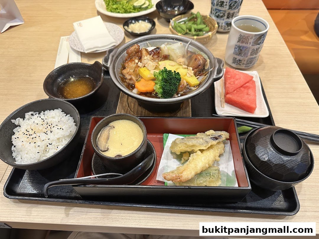 A Japanese meal set featuring teriyaki chicken, rice, tempura, chawanmushi, edamame, and watermelon.