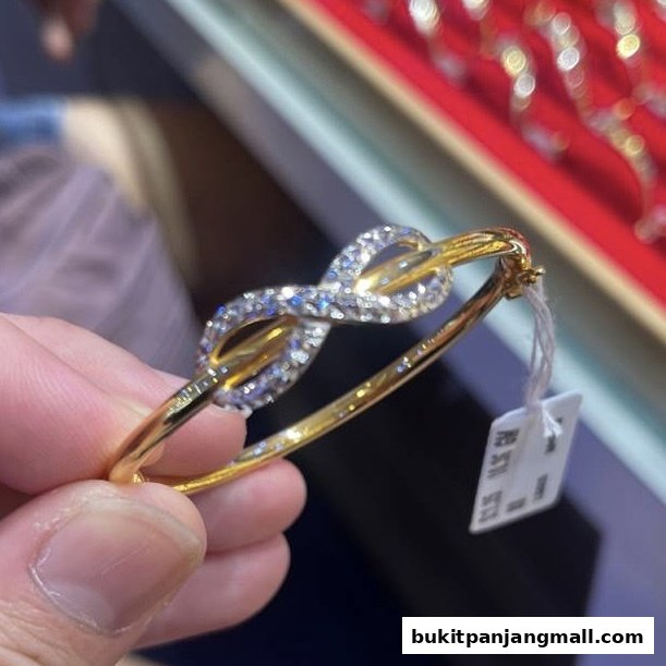 A hand holds a gold bracelet with diamond accents, featuring an infinity symbol design.