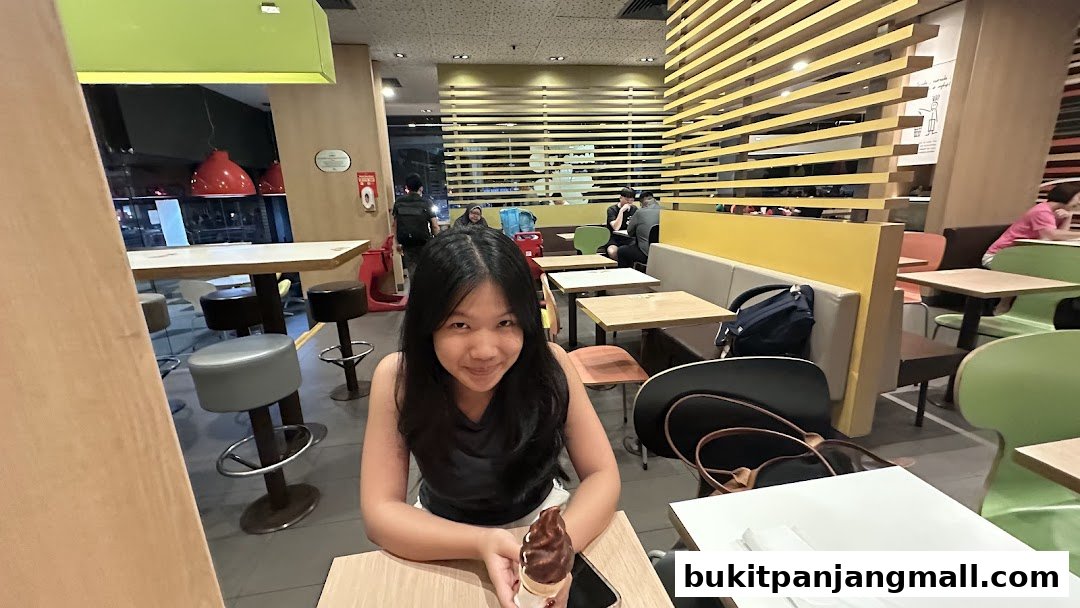 A young woman smiles holding a chocolate ice cream cone inside a McDonald's restaurant.