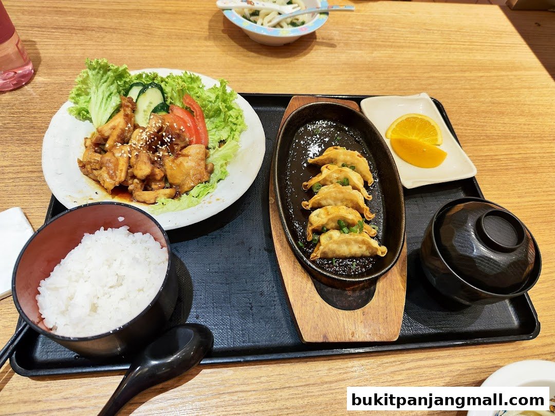 A Japanese meal set featuring teriyaki chicken, pan-fried dumplings, rice, and soup.