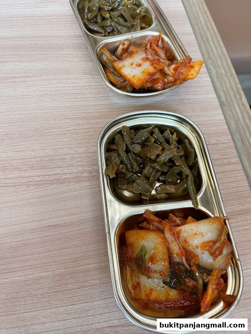 Two metal trays with Korean side dishes, including kimchi and seasoned vegetables.
