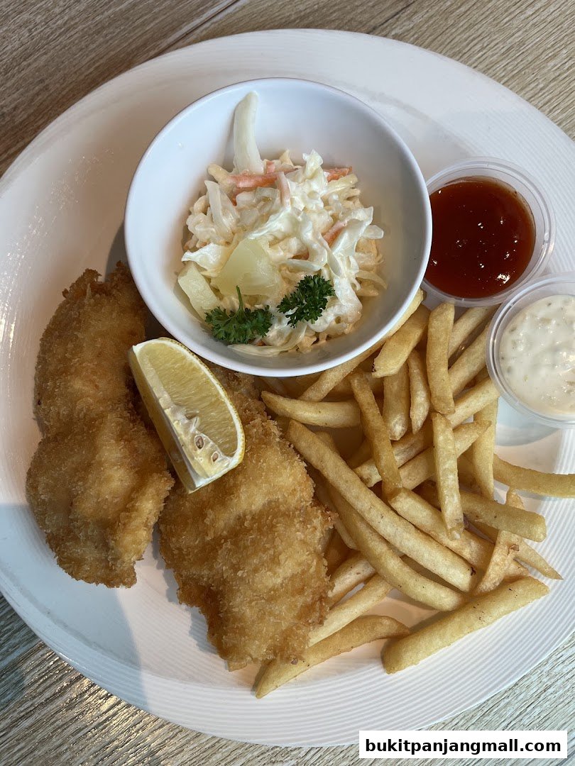 A plate of crispy fish and chips with coleslaw, lemon, and dipping sauces.