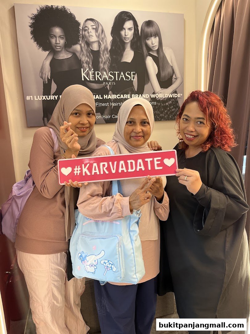 Three women pose for a photo in front of a Kérastase hair care advertisement.