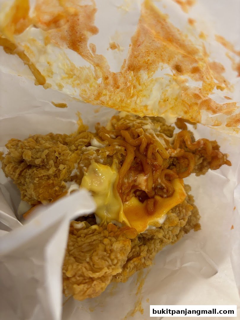 A close-up of KFC fried chicken with cheese and noodles, partially unwrapped.